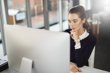 Her gün öğrenecek yeni şeyler var. Çekici genç bir iş kadını masasında oturuyor ve modern bir ofiste bilgisayar ekranına bakıyor.
