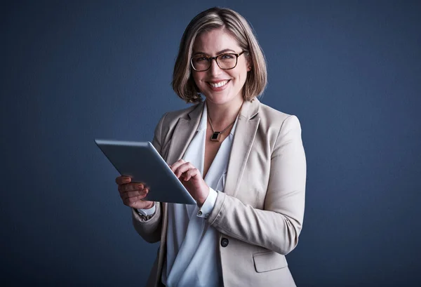 stock image Its an invaluable resource. Studio portrait of an attractive young corporate businesswoman using a tablet against a dark background