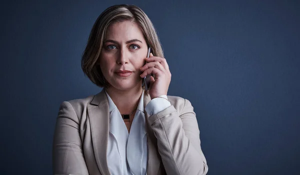 Stock image Listening intently. Studio portrait of an attractive young corporate businesswoman making a call against a dark background