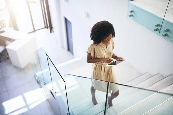 Technology helps her step up her business game. a young businesswoman using a digital tablet while walking up a staircase in an office