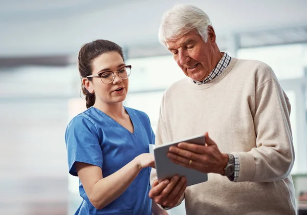 stock image All the info you need is under this tab. a young female nurse and her senior patient looking at a tablet in the old age home