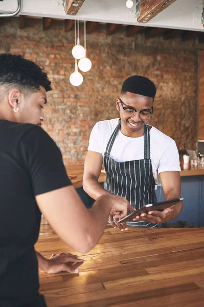 One coffee coming right up. a young man using a digital tablet while serving a customer in a cafe