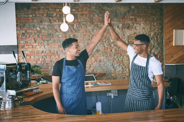 Passion brings in profit. two confident young men giving each other a high five while working in a cafe