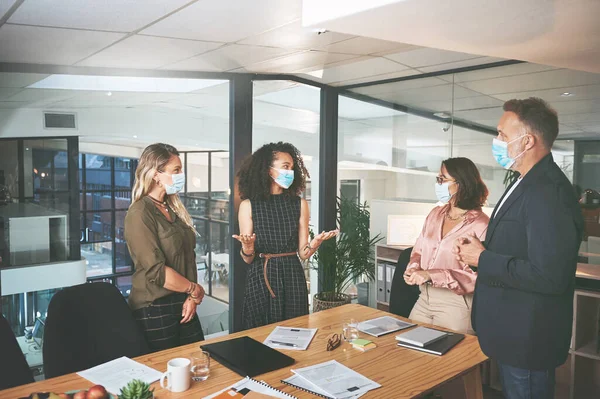 stock image Business doesnt stop just because the world did. a diverse group of businesspeople having a discussion during a meeting in the office while wearing face masks