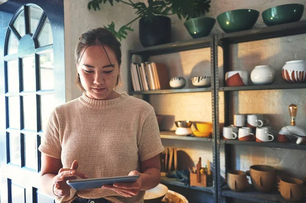 Stock image I love being busy. an attractive young business owner standing alone in her pottery studio and using a tablet