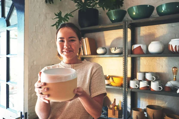 Heres your new pot. Cropped portrait of an attractive young business owner standing alone and holding a clay pot in her pottery studio