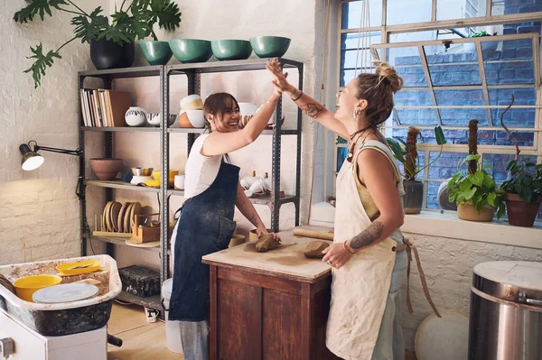 A friend in art is a friend of the heart. two young women giving each other a high five in a pottery studio