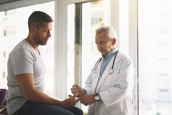 stock image Just a little prick...a senior doctor giving his male patient a thorough checkup during his consultation