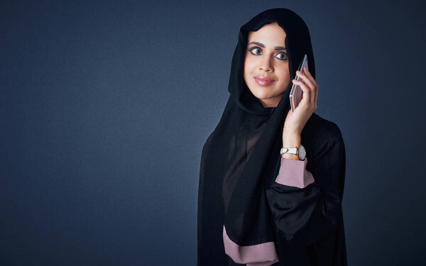 One hello could lead to something. Studio shot of a young woman wearing a burqa and using a mobile phone against a gray background