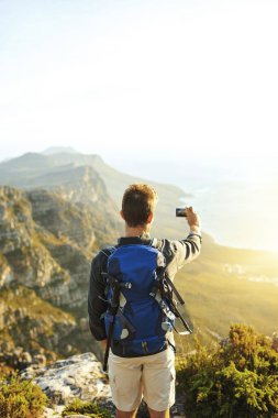 Daha güzel bir manzara bulman için sana meydan okuyorum. Genç bir adam dağa tırmanırken selfie çekiyor.