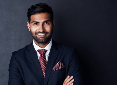 Succeeding in business with confidence and conviction. Studio shot of a confident young businessman posing against a gray background clipart