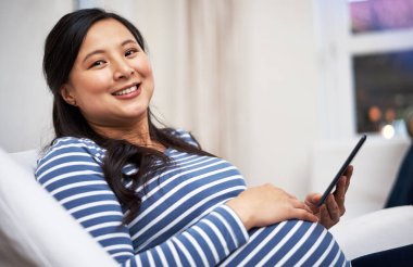 Hamilelik yolculuğumu internetten kaydediyordum. Evde dijital tablet kullanan hamile bir kadının portresi