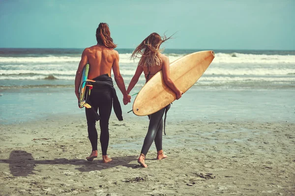 从此他们就生活在冲浪中 一对带着冲浪板在海滩上散步的年轻夫妇 — 图库照片