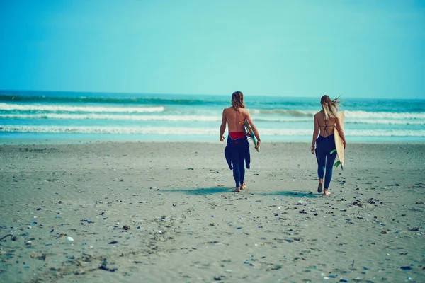 波を追うことが最優先事項です 若いカップルがサーフボードを持ってビーチを歩いていて — ストック写真