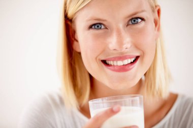 Süt, bir bardak süt içen bir kadın ve beyaz arka planda bir gülümseme. Sağlık sağlığı ya da doğal beslenme, sağlıklı ve kadın insan, mutlu bir yüzle stüdyo arka planında gülümseyen bir içki içer..