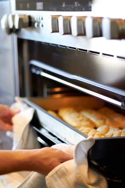 Hands, closeup and tray from oven for bread, baking product or food for small business, cafe or restaurant. Chef, baker or person with cloth for safety in bakery, coffee shop or food industry startup.