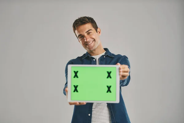 技术在我们如何保持联系中起着一定的作用 一个年轻男子拿着一个绿色屏幕的数码平板电脑 灰色背景的工作室肖像 — 图库照片