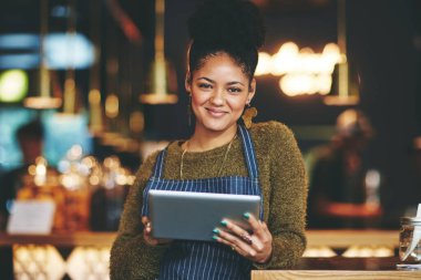 Akıllı teknoloji kahve dükkanı yönetimini çok daha kolaylaştırıyor. Bir kafede çalışırken dijital tablet kullanan genç bir kadın.