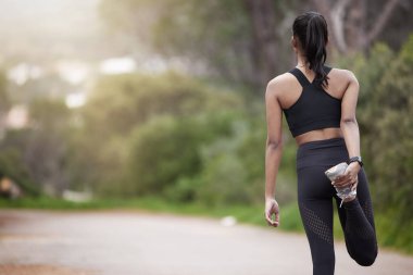 Doğa, kadın ve arkadan ısınma, bacak esnetirken motivasyon ve zindelik. Adanmışlık, bağlılık ve kız koşucu yolda ayakta durarak koşmak ve antreman yapmak için