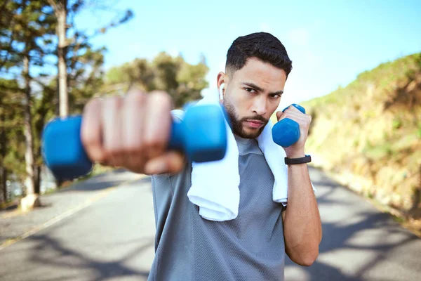 Man, dumbbell and punches in nature fitness for exercise, workout or training in the outdoors. Portrait of fit, active and sporty male person punching with weights in healthy outdoor cardio endurance.