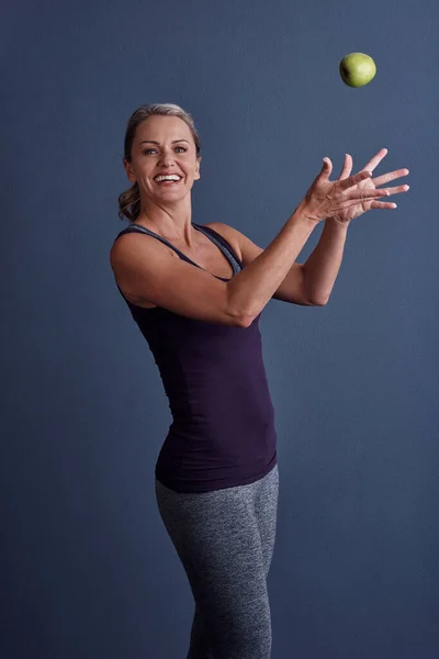 stock image All you have to do is grab it. Studio portrait of an attractive mature woman throwing an apple against a blue background