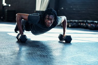 Ancak devam edersem zindeliğim düzelir. Spor salonunda dambıllarıyla şınav çeken genç bir adam.