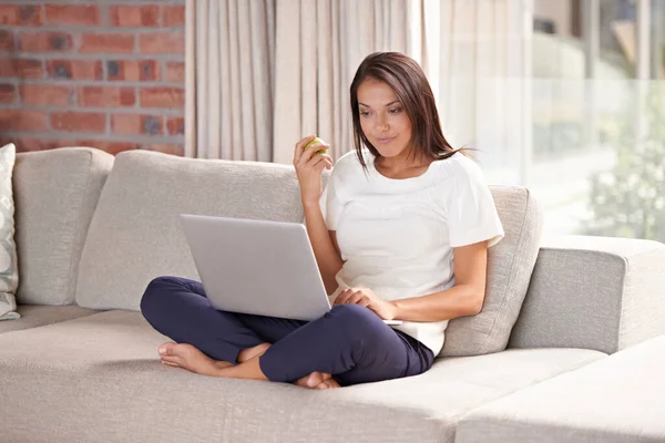 사과먹기 노트북먹기 소파에서 이메일읽기 온라인으로 스트리밍하기 여성은 소파에서 작업을 과일로 — 스톡 사진