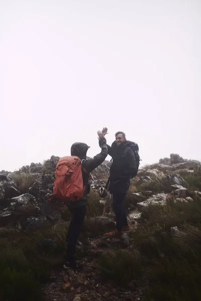 冲过去是你爬上山顶的唯一途径 两个男的在登山时互相击掌庆祝 — 图库照片
