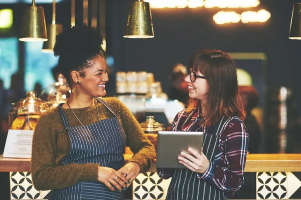 stock image Arranging their shifts for the week. two young women using a digital tablet together while working at a coffee shop