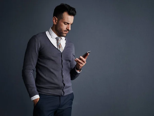 Increasing productivity by staying connected. Studio shot of a stylish young businessman using a mobile phone against a gray background