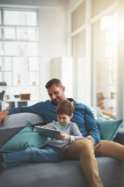 stock image Kids these days like their technology. a cheerful little boy browsing on a digital tablet while lying on his fathers lap at home during the day