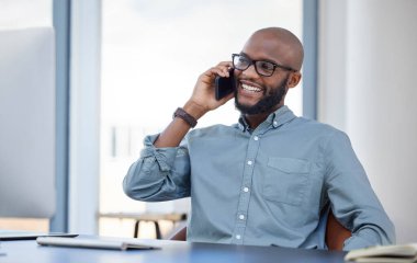Mutlu, akıllı telefonu olan bir iş adamı ve iş yerindeki bilgisayarla masasında bir telefon görüşmesi yapıyor. Çevrimiçi iletişim, gülümseme ve cep telefonuyla modern çalışma alanında konuşan Afrikalı adam..