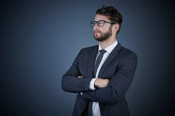 企業経営の顔 暗い背景を背景に腕を組んで立っているハンサムな若いビジネスマンのスタジオショット — ストック写真