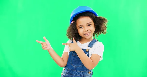 Kids, construction and a girl on a green screen background in studio pointing at building space. Children, architecture and design with a cute female child engineer wearing a hardhat on chromakey.