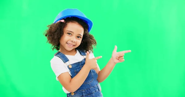Children, construction and a girl on a green screen background in studio pointing at building space. Kids, architecture and design with a cute female child engineer wearing a hardhat on chromakey.