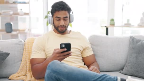 自宅でソファの上で音楽を聴いているヘッドフォン 男はリラックスして幸せ ラウンジの男性の家 ウェブラジオ オーディオストリーミングとソファの上のモバイルのリビングルーム — ストック動画