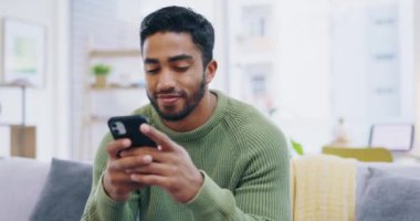 Telefon, rahatlama ve evdeki sosyal medya, ağ kurmak ve mobil uygulama sohbetleri için oturma odasındaki koltukta oturan mutlu adam. İletişim kuran, internetten kitap okuyan ve kanepede ya da dinlenme odasında internet paylaşan genç Hintli..