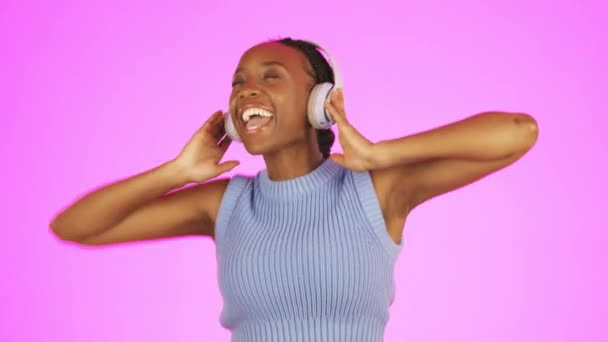 ピンクのスタジオの背景に対して勝利 割引または販売のためのお祝いの音楽を聞いて黒人女性 ダンスおよびヘッドフォン 幸せな隔離されたアフリカ系アメリカ人女性オーディオへのダンスを楽しむ — ストック動画