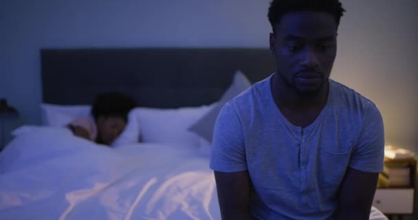 不妊症 うつ病 黒人男性がベッドの上に座り 妻は夜寝ていました 勃起不全 不貞と彼の家の寝室で悲しい感じの夫と眠れない — ストック動画