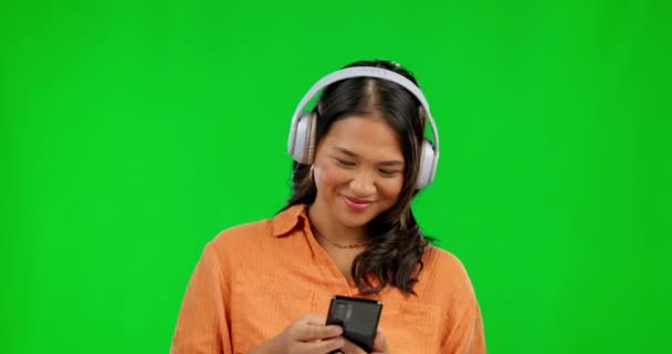 背景のモックアップに隔離されたスタジオで緑の画面上の音楽のヘッドフォン ラジオ 聞くと入力するためのスマートフォンでアジアの人 ソーシャルメディアやストリーミングポッドキャストでスクロール — ストック動画