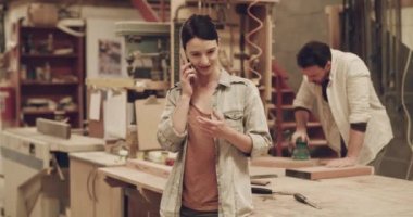 Telefon, kadın ya da marangoz bir atölyede küçük işletme planlaması için konuşuyor. Marangozluk anlaşması, geliştirme ve yaratıcı mobilya projesi için akıllı telefondan konuşan bir kadın..