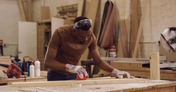 デザイン プロの木工のための彼の工場で木材の板を測定男 安全ゴーグル 彼のワークショップでは テープ測定を使用して男性大工との手作業と専門知識 — ストック動画