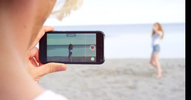 女性のインフルエンサーのためのソーシャルメディアダンス ビーチや電話 夏の休日に投稿または記録 女の子のダンサーとビデオブログのためのスマートフォン ダンスの傾向や海の砂によるライブストリーミングのためのアプリ — ストック動画