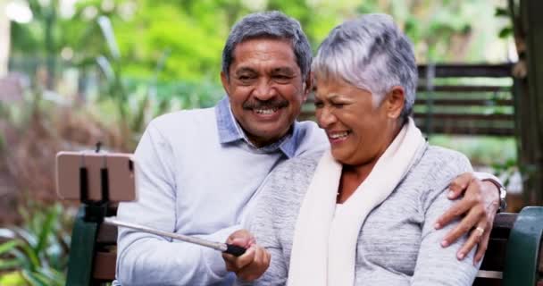 老夫妇 自拍和笑在公园里与关怀 爱和粘连在长椅上的社交媒体应用 老年男子 老年妇女和退休人士 享受摄影 照片或博客带来的快乐 — 图库视频影像