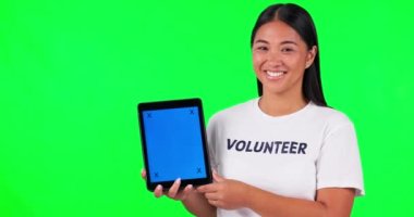 Tablet, hey sen ve bir kadın stüdyoda yeşil ekran arka planında gönüllü olarak izleme işaretleri olan bir ekran tutuyorsunuz. Portre, hayır kurumu sitesi ve elinde kromakey tutan mutlu bir Asyalı..