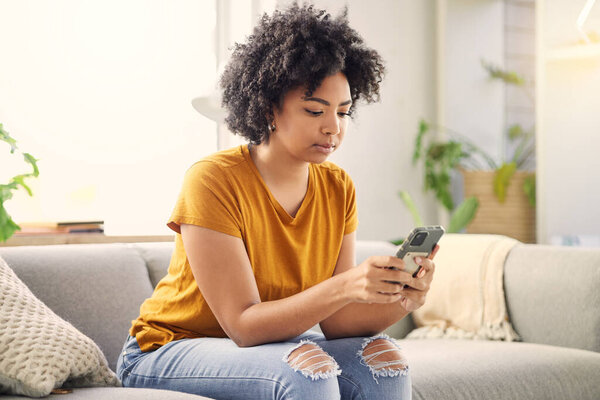 Phone, relax and woman on sofa in home living room for social media, internet scroll or texting. Mobile, serious or African person on couch in lounge for online app, website or reading email in house.