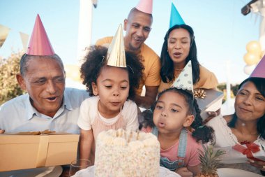 Aile, doğum günü ve kız eğlence olsun diye parti şapkalarıyla mum üflüyor. Mutluluk, çocuk ve pasta ile bir dilek tutun ya da çocuklar, dışarıda özel bir etkinlik için büyükanne ve büyükbaba