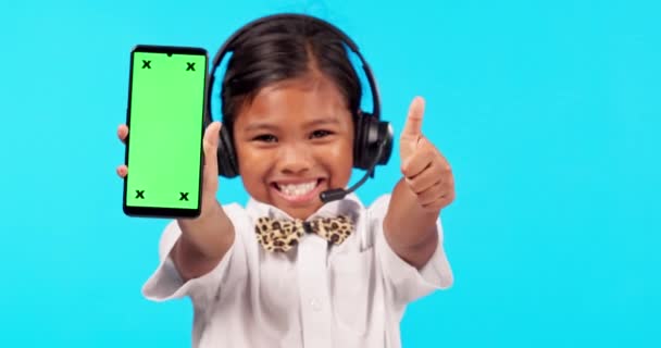 女孩的肖像与智能手机和耳机与她的大拇指在蓝色背景下成功 成绩或模仿 营销或广告以及使用手机的年轻女性 — 图库视频影像