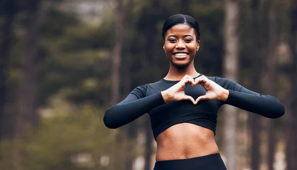 Heart hand, black woman and fitness in nature with exercise and fitness with love gesture. Sport, female person and support outdoor by the trees after a run with romance sign from a workout in park.