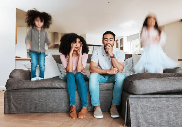 Children jumping with stressed parents on the sofa to relax in the living room of their house. Upset, burnout and excited kids playing with blur motion on couch with tired exhausted mother and father.